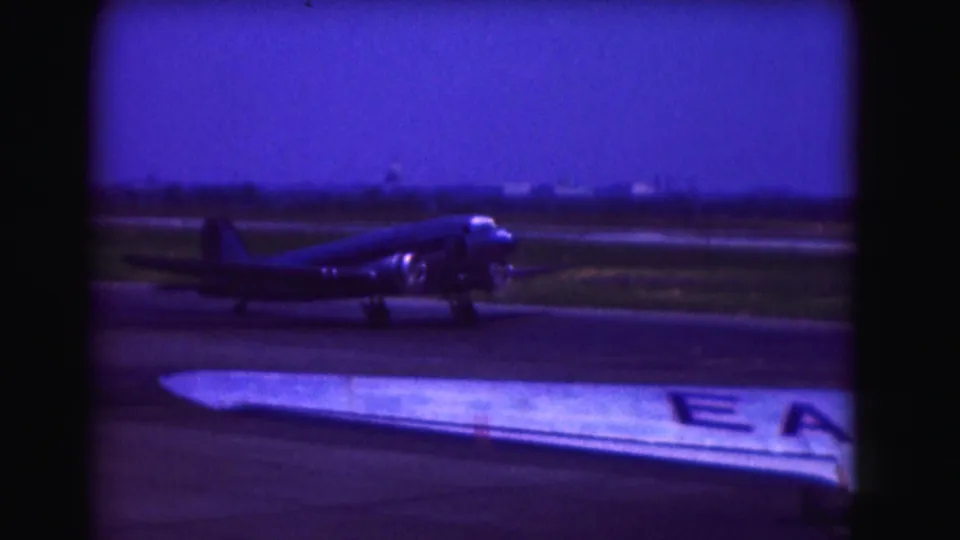 1975 Washington, DC-area home-movie frame showing a propeller airplane on the tarmac, seen past a foreground aircraft wing.