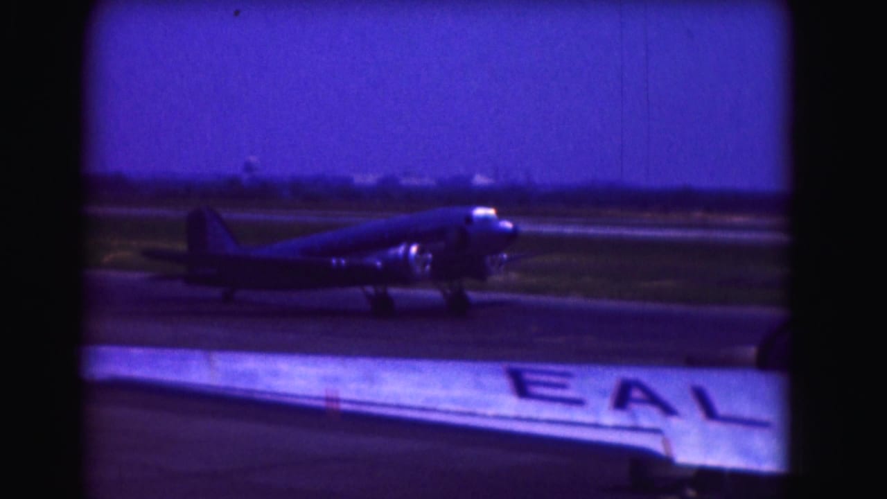 Propeller airplane beside a runway, partly obscured by the wing of another aircraft.