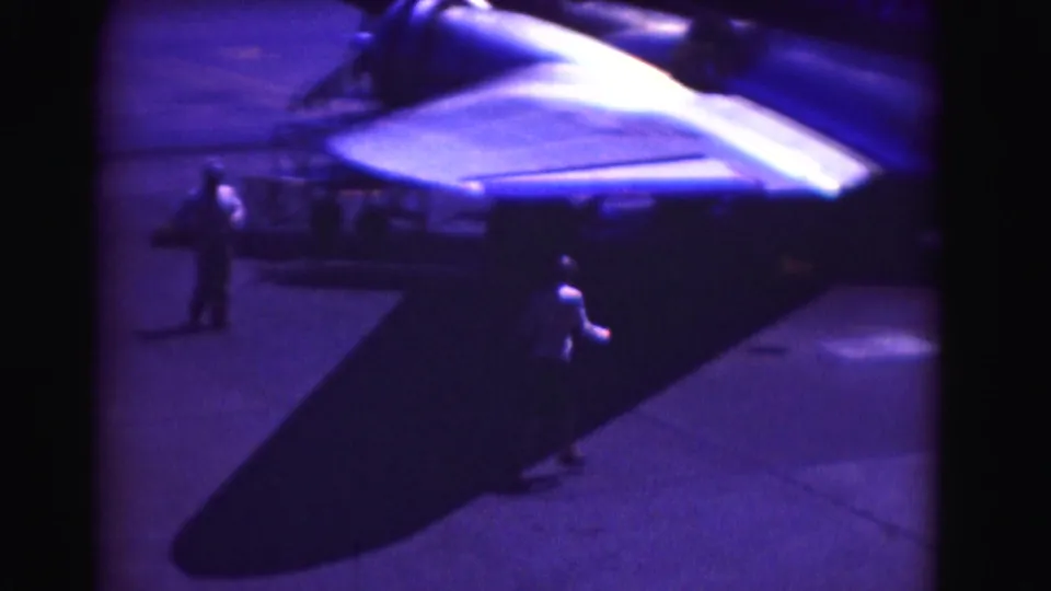1975 Washington, DC-area tarmac frame with people near a parked aircraft wing and a large shadow across the pavement.