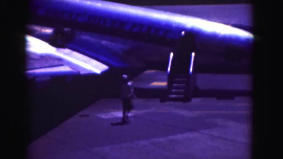 1975 Washington, DC-area home-movie frame showing an aircraft fuselage, open stairs, and a person standing on the tarmac.