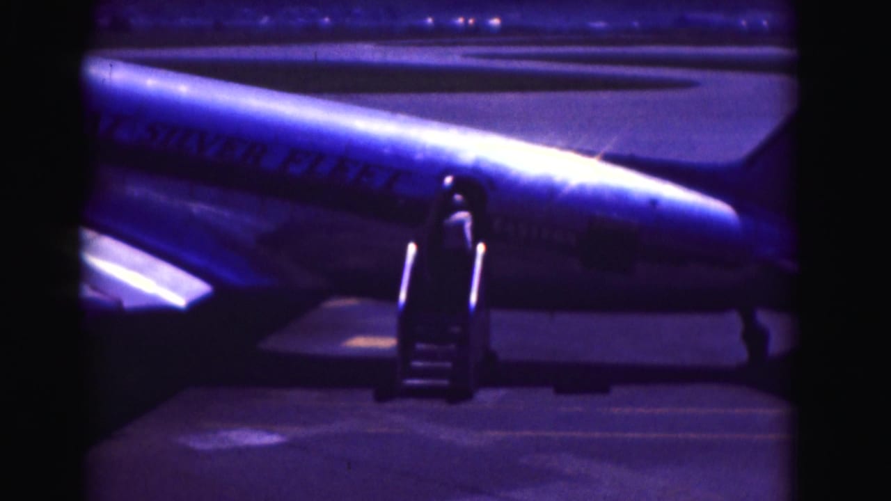 Portable boarding stairs positioned against a Pan Am jet under blue night light.