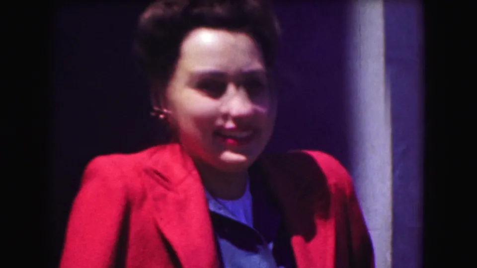 1975 Washington DC frame of a smiling woman in a red blazer, filmed close to the camera with strong contrast and home-movie softness.
