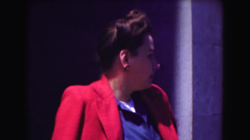 The woman in the red jacket is seen in profile near a column, turning away from the camera in 1975 Washington, DC footage.