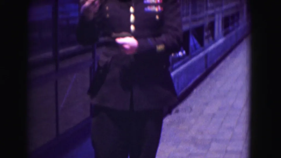 Close 1975 home-movie view of a uniformed officer's torso and hand as he appears to retrieve or hold an item near his pocket.