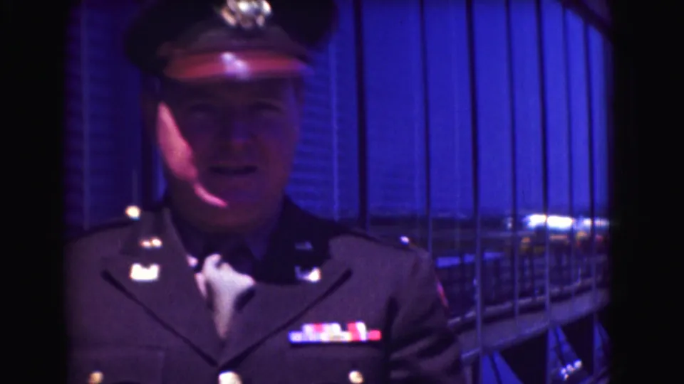 Closer 1975 Washington DC frame of the uniformed man facing the camera, with cap, collar insignia, and ribbon bars visible.