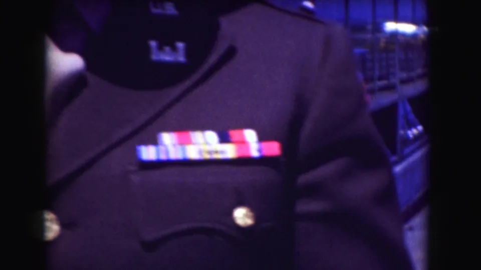 Close 1975 Washington DC view of colorful award ribbons on a dark military-style jacket, with the man's cap and shoulder partly visible.