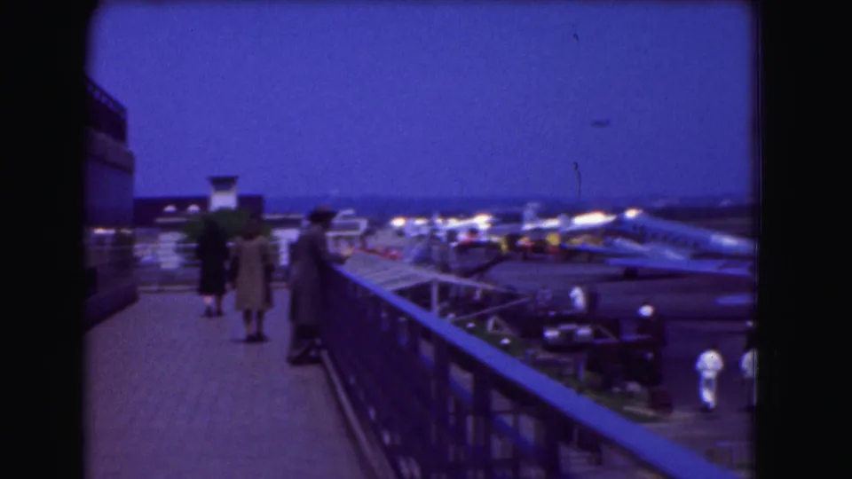 Onlookers on a 1975 Washington DC observation platform watch aircraft and ground activity at an airport or air base.