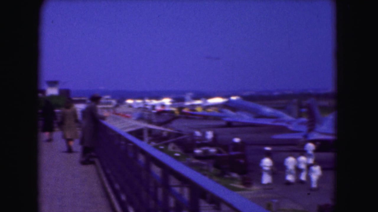 Passengers on an observation deck look toward aircraft parked on an airport tarmac.
