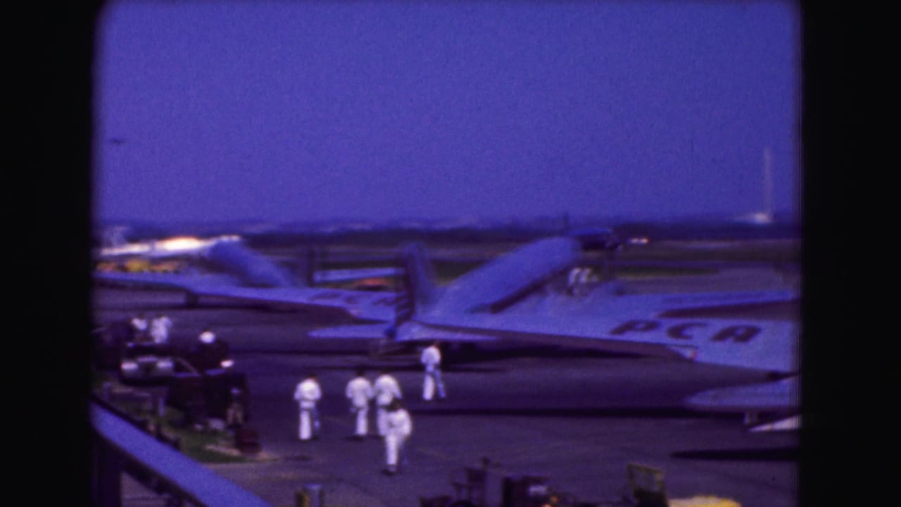 Ground crew in white uniforms stand near aircraft parked on the tarmac.