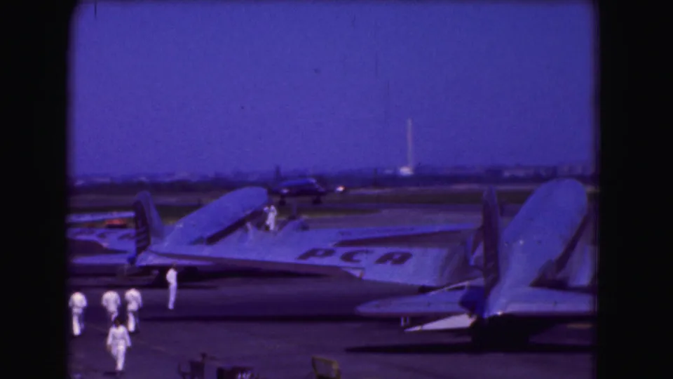 1975 Washington DC frame showing a large aircraft with visible markings, nearby crew, and another aircraft behind it on the airport tarmac.