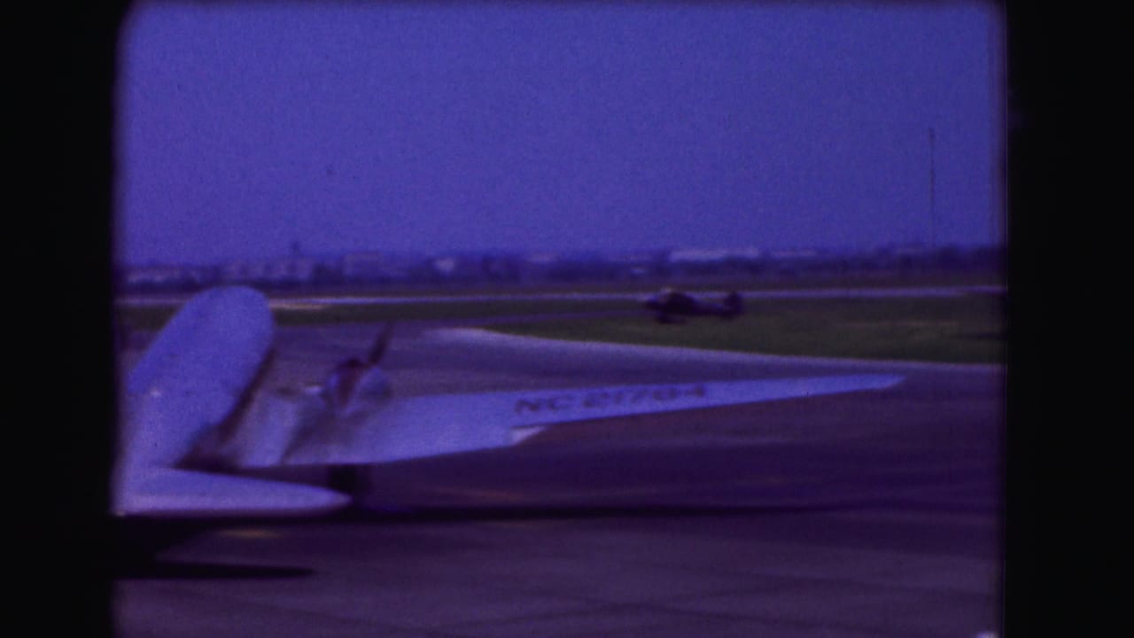 1975 Washington DC home-movie frame showing part of a large propeller airplane on a tarmac, with runway grass and dark vertical framing.