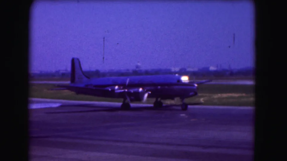 Side view of a large propeller airplane taxiing on a Washington DC tarmac in 1975, with visible grain, soft focus, and faded color.