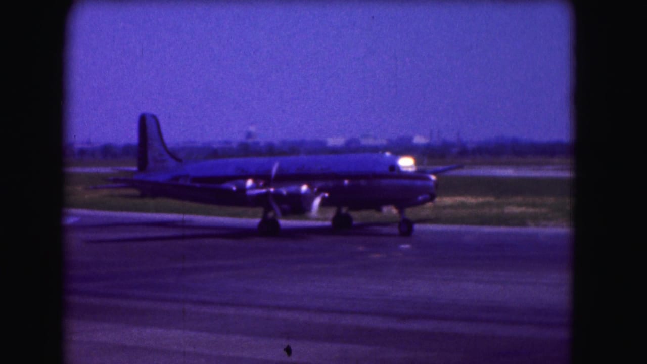1975 Washington DC home-movie frame showing a propeller-driven airliner taxiing across airport pavement.