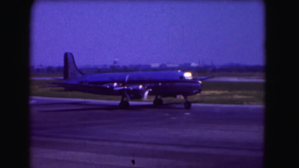 1975 Washington DC home-movie frame showing a propeller-driven airliner taxiing across airport pavement.