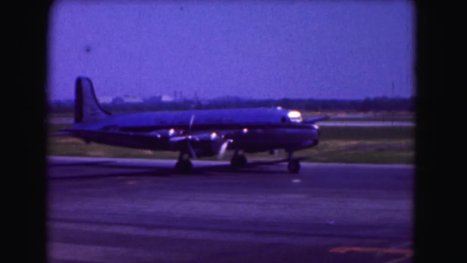 Blue-purple 8mm frame of a propeller-driven airliner in profile on a Washington DC runway in 1975.