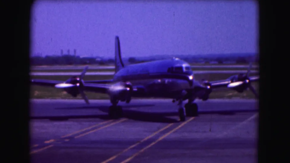 1975 Washington DC home-movie frame showing the airliner from the front at an angle, with taxiway lines leading toward it.