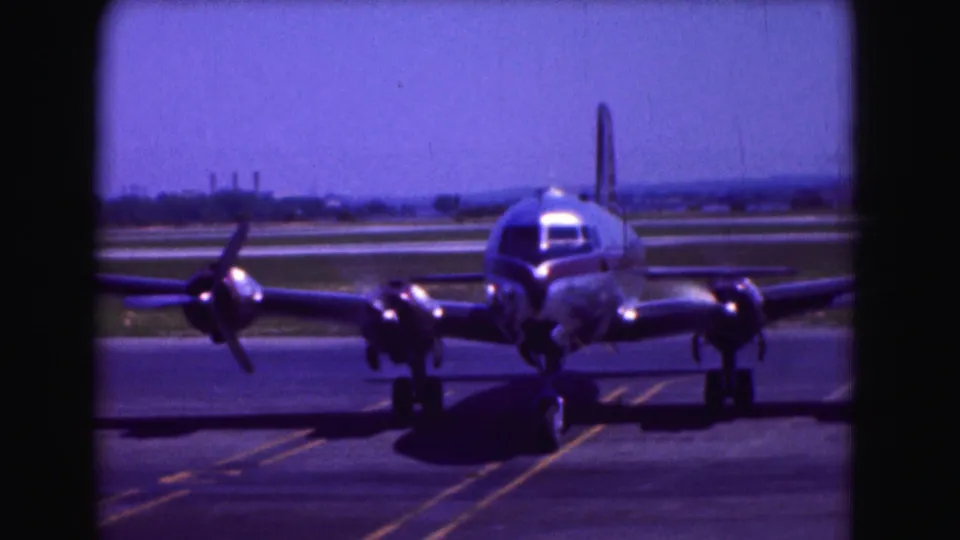 Closer 1975 Washington DC frame of a four-propeller passenger aircraft taxiing on an airport runway.