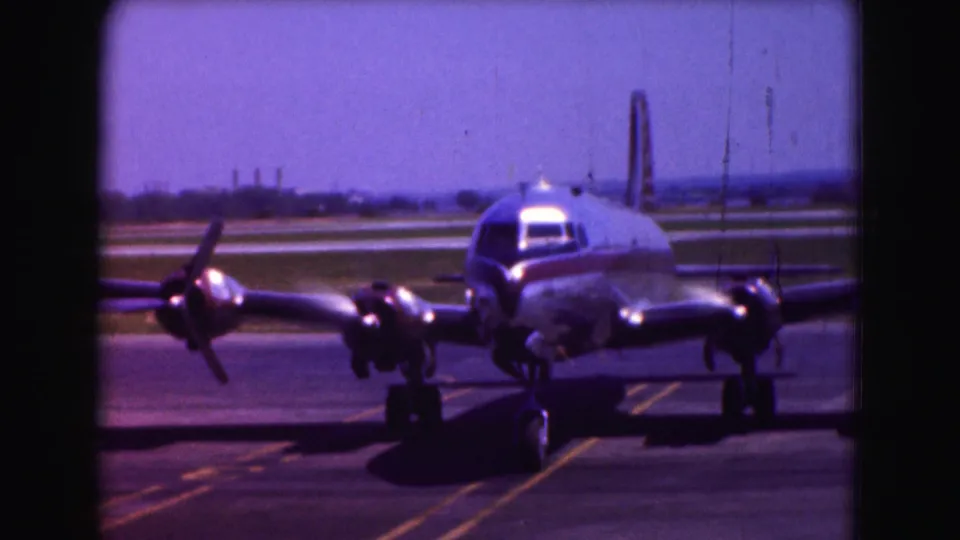 1975 Washington DC 8mm frame showing a silver propeller passenger plane angled slightly as it taxis.