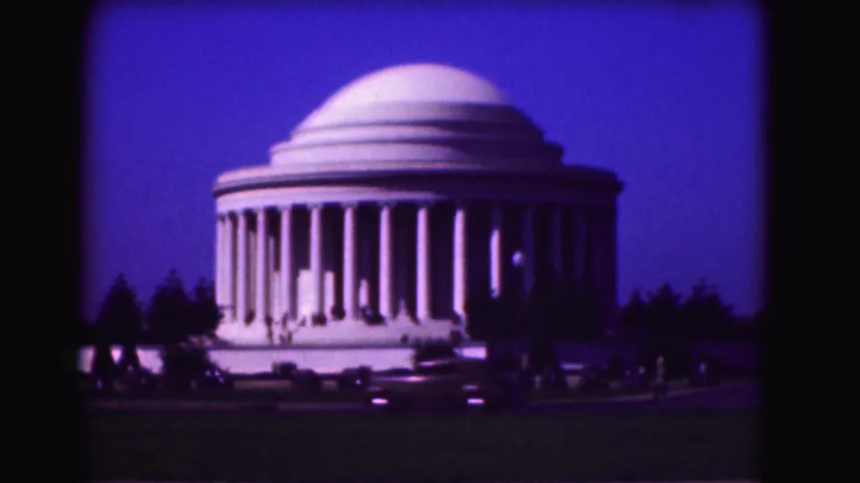 1975 8mm view of the Jefferson Memorial in Washington, DC, with a blue evening sky, small visitors, lawn, and passing cars.