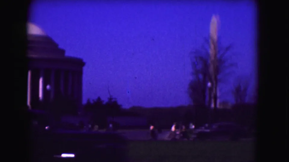 Washington, DC landmark view with the Jefferson Memorial at left, the Washington Monument at right, lawn, traffic, and twilight sky.