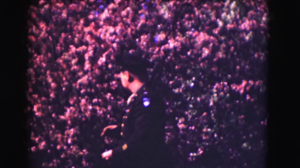 A uniformed police officer moves along the hedge line in the 1975 Washington DC home-movie scene.