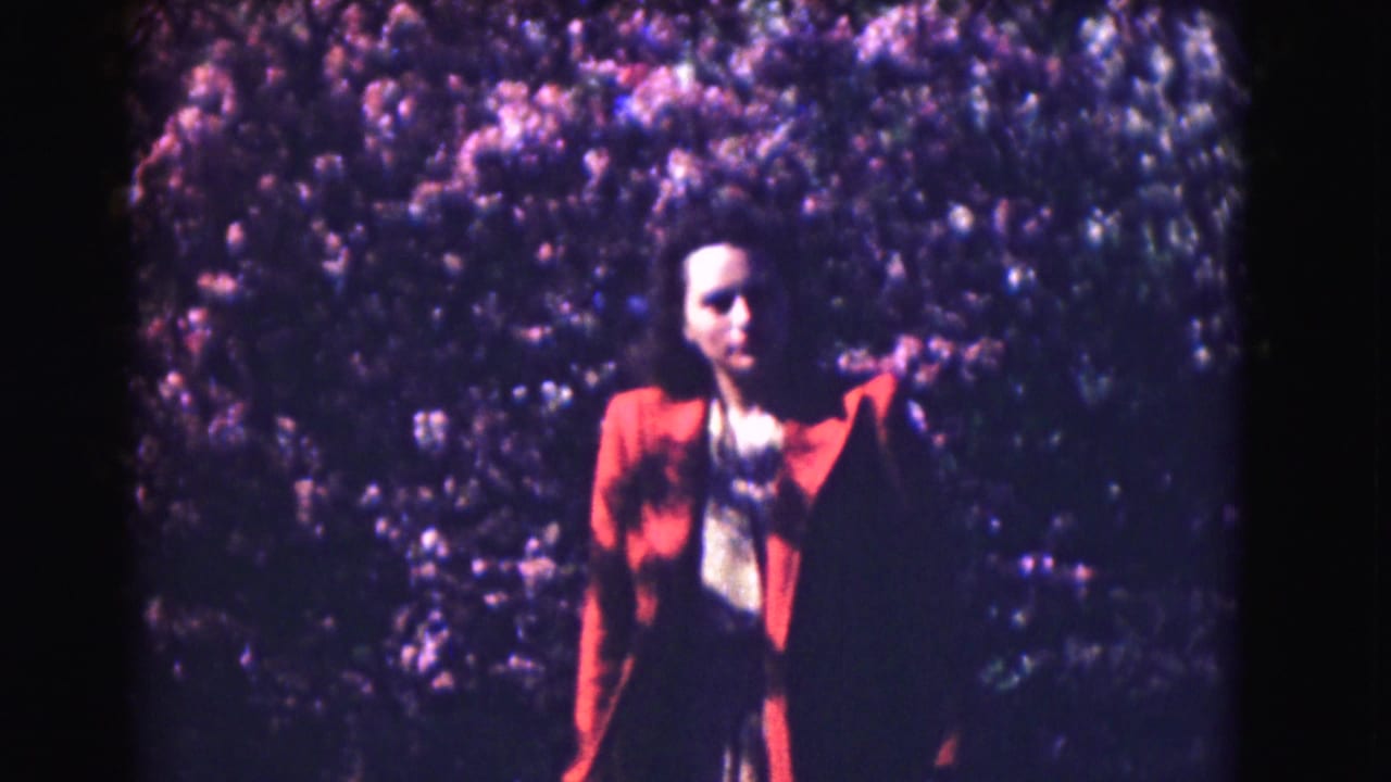 1975 Washington DC home-movie frame of a woman in a red jacket posing in front of pink flowering trees.
