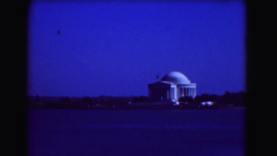 1975 8mm frame showing the Jefferson Memorial across the Tidal Basin, with blue night exposure and silhouetted shoreline trees.