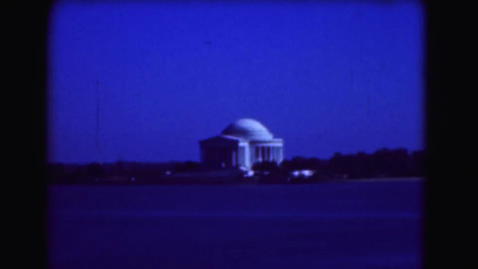 Washington, DC 1975 home-movie frame of the Jefferson Memorial across water, with the building isolated against a deep blue sky.