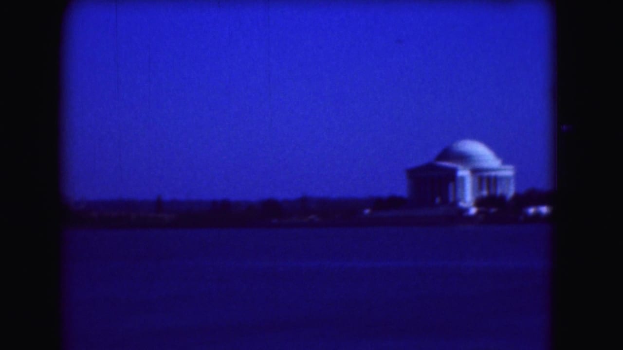 Blue-tinted distant view of the Jefferson Memorial across water.