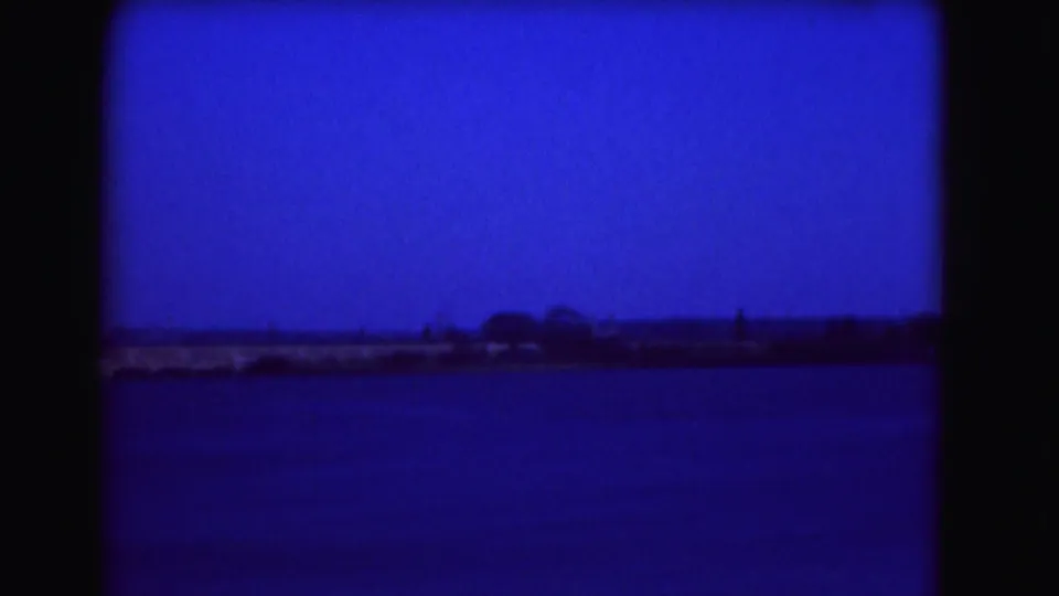 Blue-tinted 1975 Washington DC frame looking across the Tidal Basin toward a low shoreline with trees in the distance.