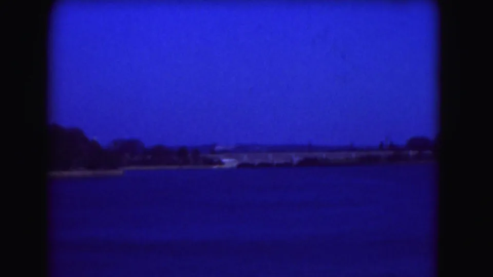 1975 Washington DC home-movie frame showing the Tidal Basin and a distant tree-lined shore under a heavy blue color cast.