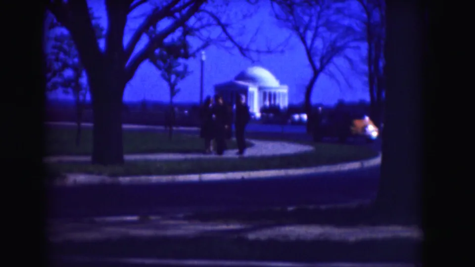 1975 Washington DC home-movie frame with visitors on a path near the Jefferson Memorial, trees, and an automobile in the background.