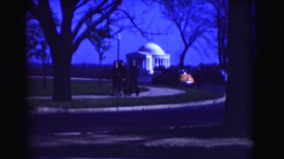 1975 Washington, DC home-movie frame showing people by a sidewalk, a passing car, bare trees, and the Jefferson Memorial in the distance.