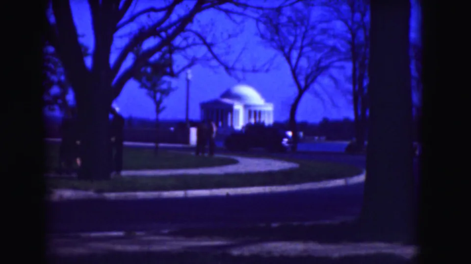 1975 Washington, DC home-movie frame showing the Jefferson Memorial beyond bare trees, with pedestrians and a car along the road.
