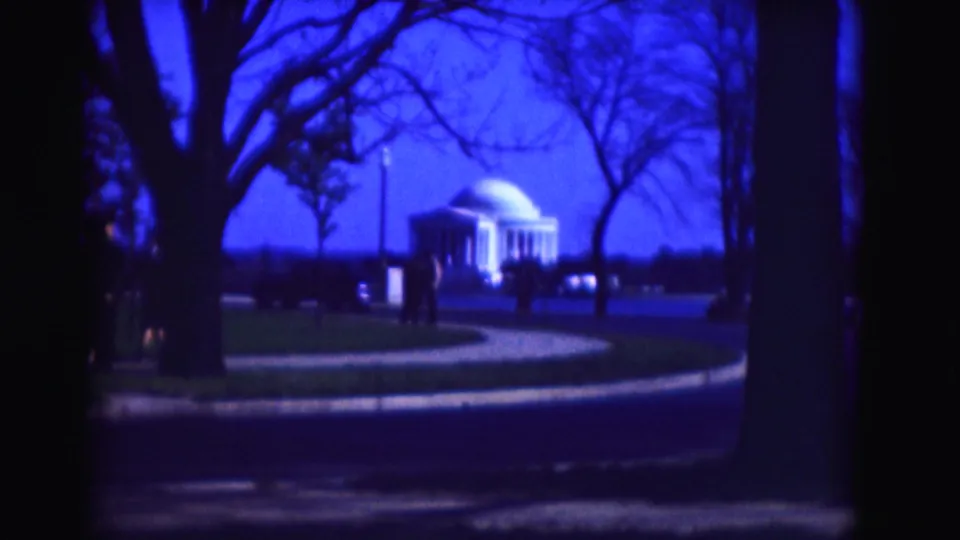 1975 8mm Washington, DC view of the Jefferson Memorial in the distance, framed by leafless trees, lawn, and a winding path.