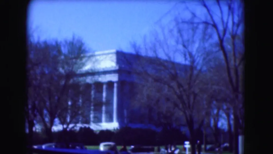 Blue-tinted 1975 Washington, DC home-movie frame showing a neoclassical building near the memorial grounds behind leafless trees.