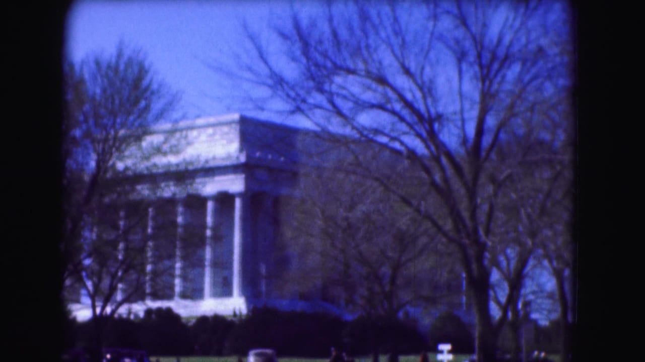 1975 8mm view of the Lincoln Memorial in Washington DC framed by bare winter trees and dark shrubs.