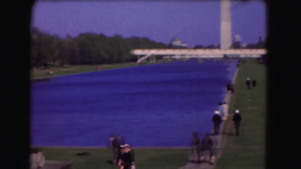 1975 Washington, D.C. home-movie frame showing visitors near the Reflecting Pool, the Washington Monument, lawns, trees, and distant civic buildings.