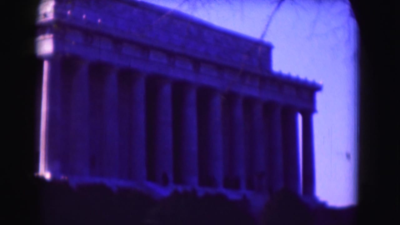 Angled 1975 home-movie view of the Lincoln Memorial in Washington, DC, with the colonnade, dark shrub line, and tinted sky visible.