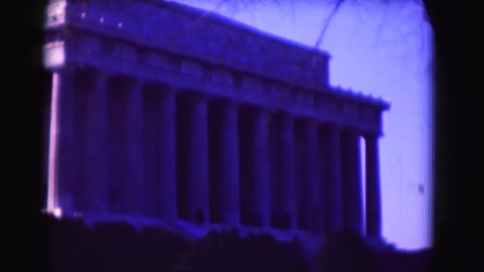 Angled 1975 home-movie view of the Lincoln Memorial in Washington, DC, with the colonnade, dark shrub line, and tinted sky visible.