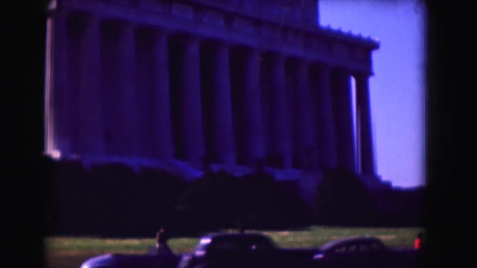 1975 8mm view of the Lincoln Memorial in Washington, DC, with foreground lawn, small visitors, and cars visible below the columns.