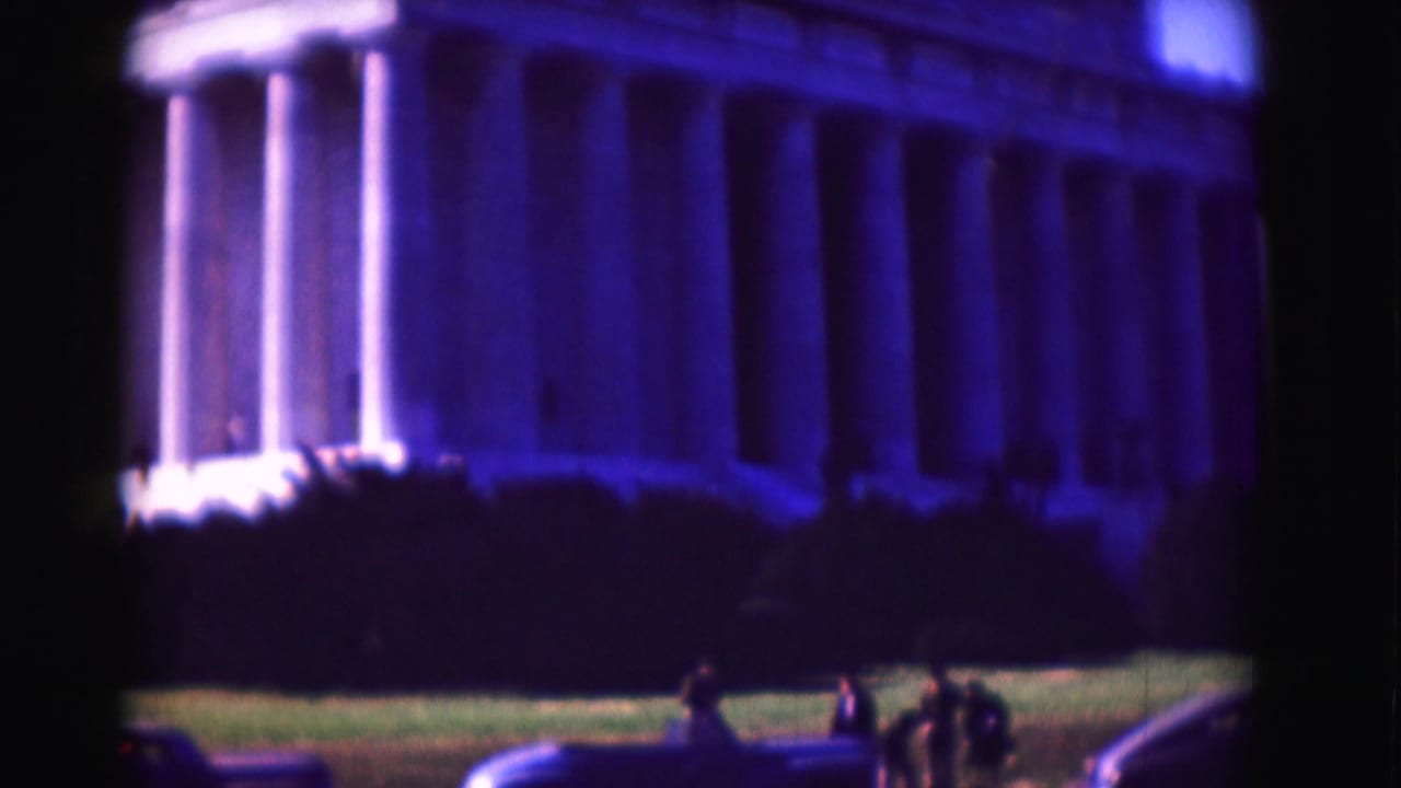 Lincoln Memorial columns seen beyond lawn, cars, and small visitors.