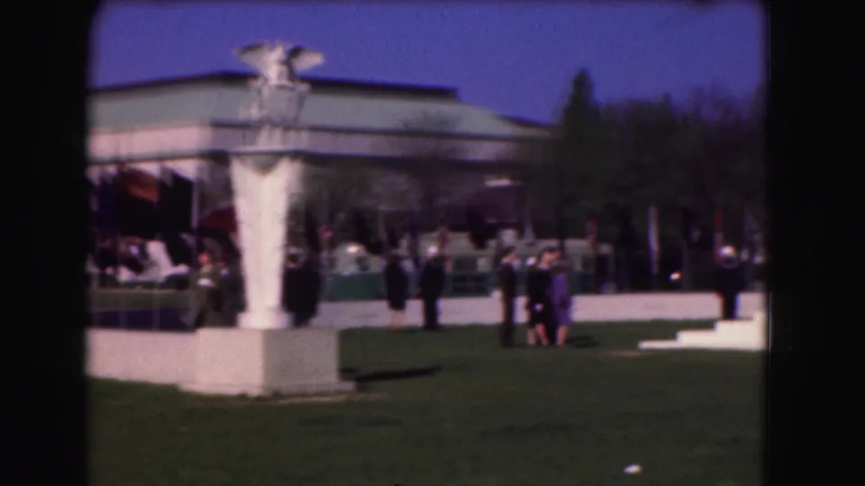 1975 visitor-shot view of the memorial grounds, showing people on the lawn and a white statue or fountain form near buildings.