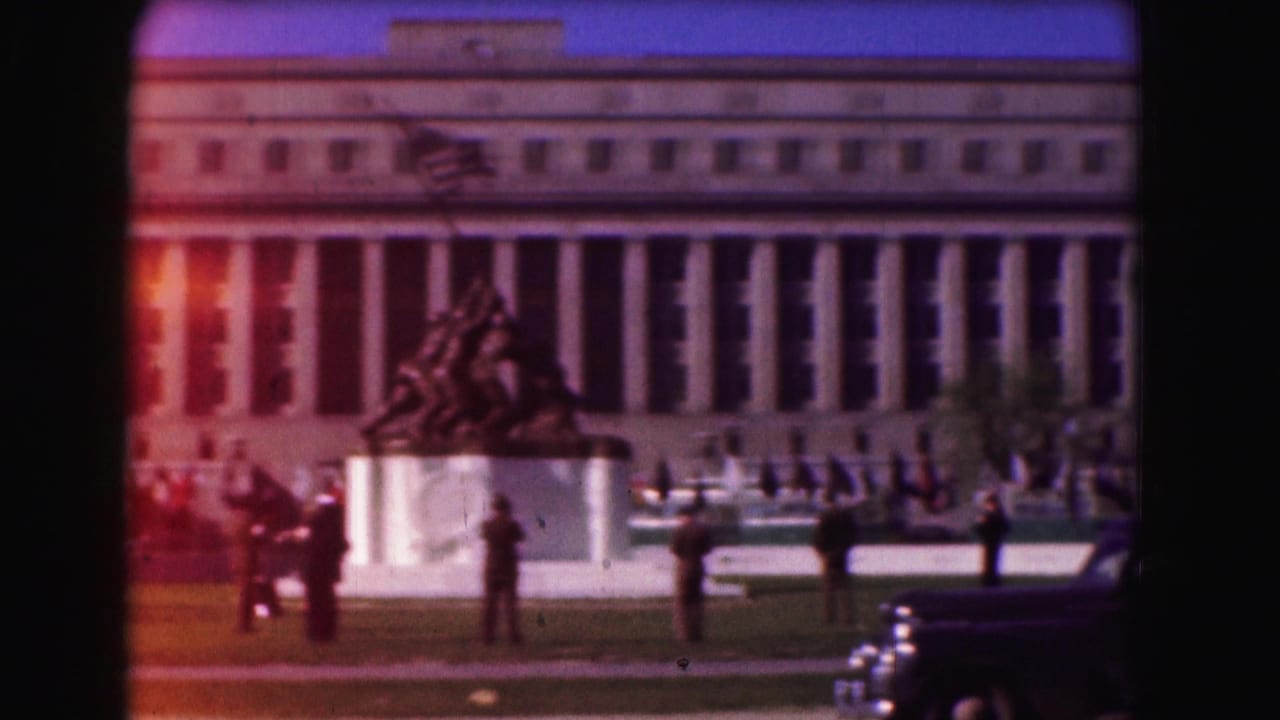 Iwo Jima statue before a columned government building with people and cars nearby.