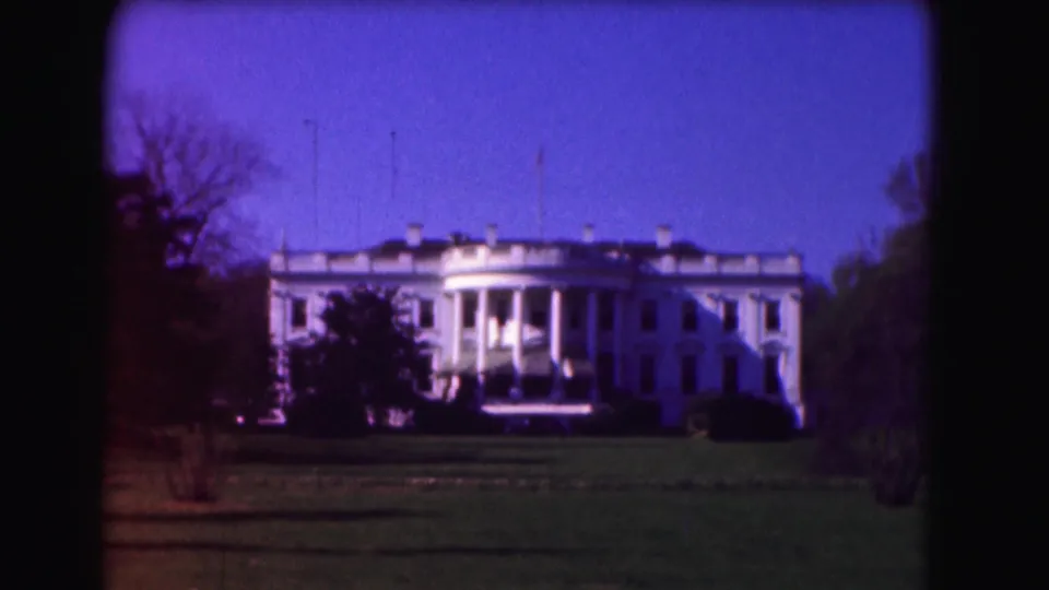 1975 Washington, D.C. home-movie view of the White House from across the lawn, framed by trees and open sky.