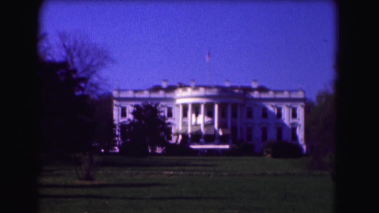 Distant White House view across a lawn with trees and blue sky.