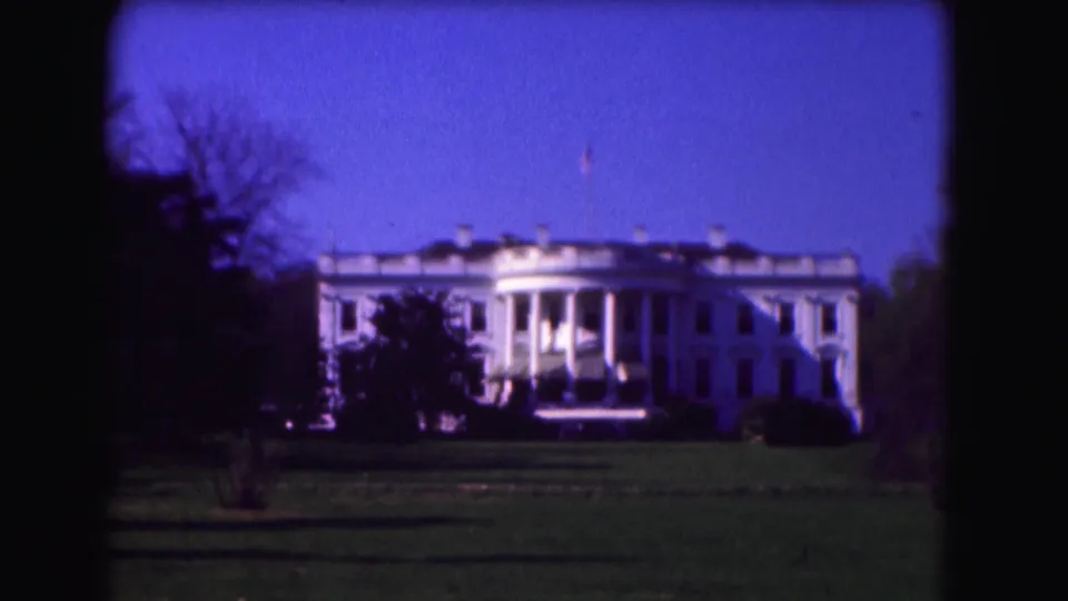 1975 8mm view of the White House in Washington, D.C., seen across the lawn with trees framing the building.
