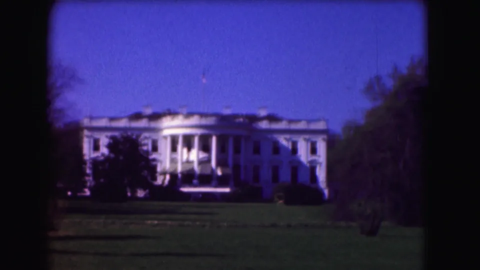 1975 8mm view of the White House and lawn in Washington, D.C., with trees and dark film-frame borders visible.