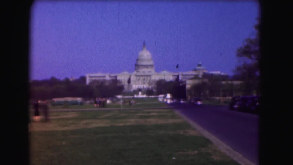1975 8mm view toward the U.S. Capitol in Washington, D.C., seen across lawn and roadway with small groups of pedestrians.