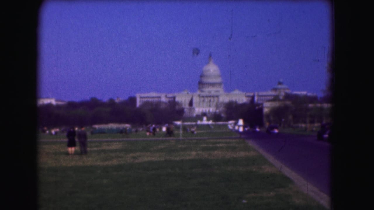 A distant 1975 view of the U.S. Capitol from the Mall, with pedestrians on the lawn and a roadway leading toward the building.